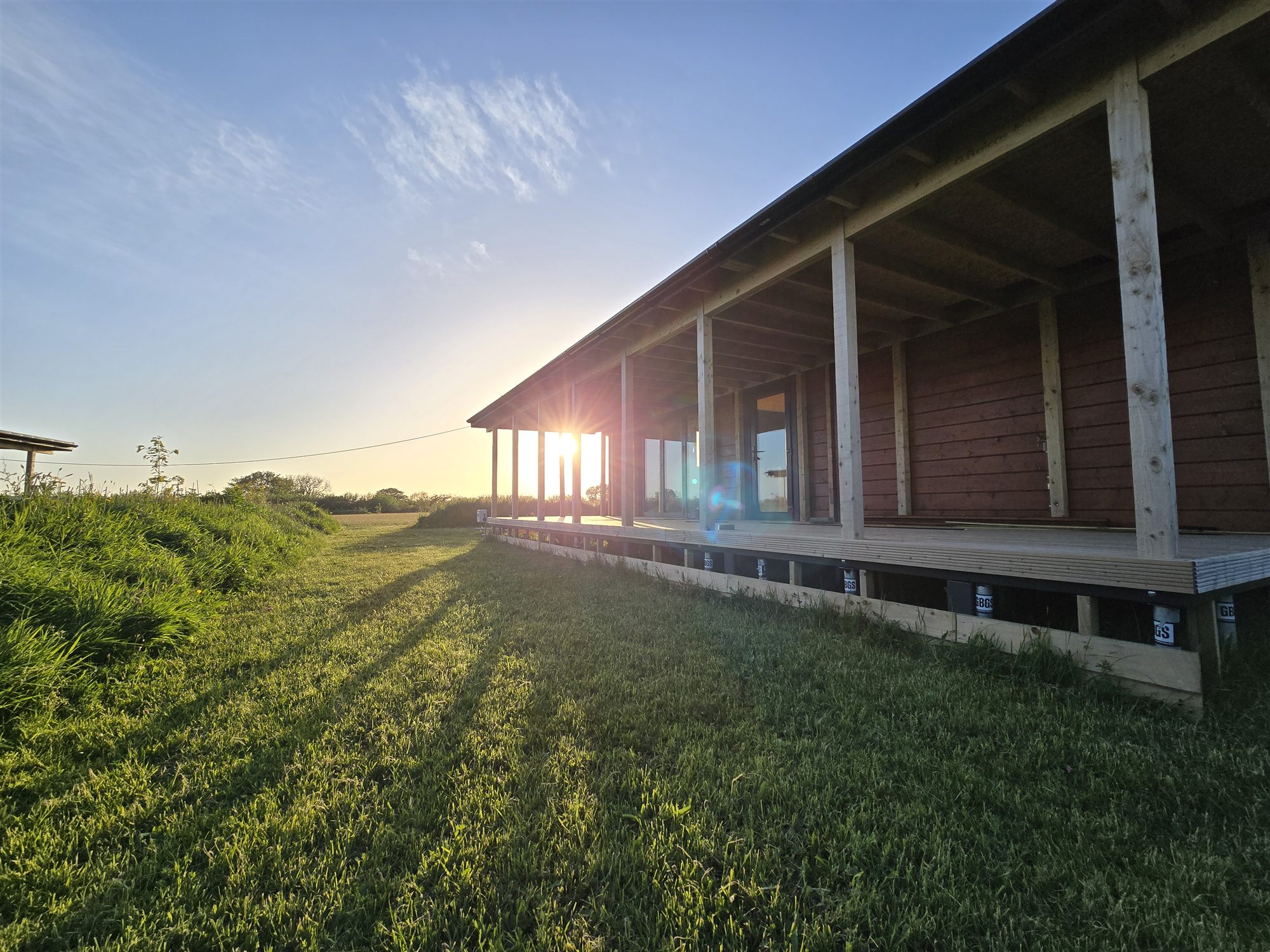 Golden evening light across a lodge and meadow at Carreg Gamu Glamping.